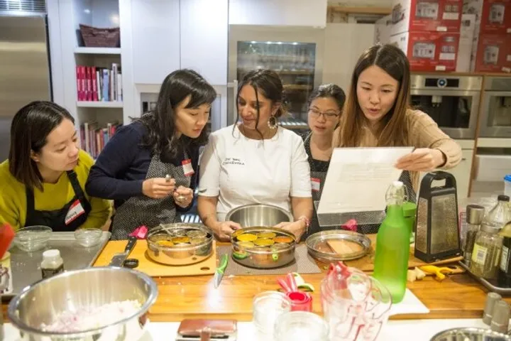 Group of women in an Indian cooking class, focused on preparing dishes and sharing instructions in a vibrant kitchen.