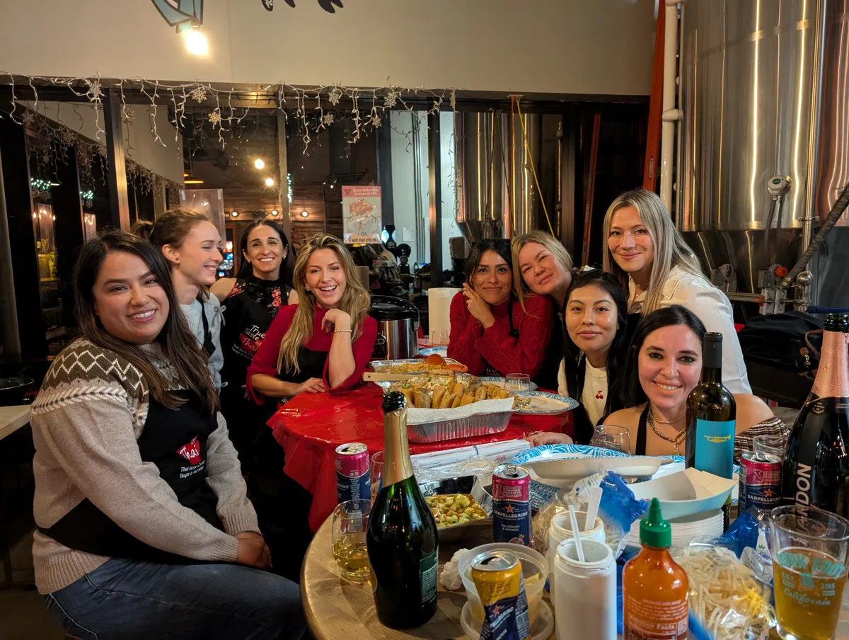 Group of women smiling around a table during an Authentic Pad Thai cooking class in San Diego, enjoying food and drinks.