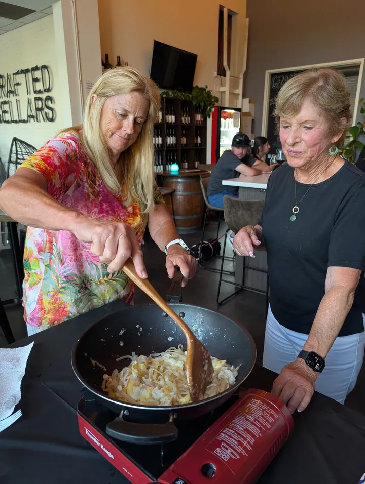 Two women cooking together in a wok during an Authentic Pad Thai class in San Diego.
