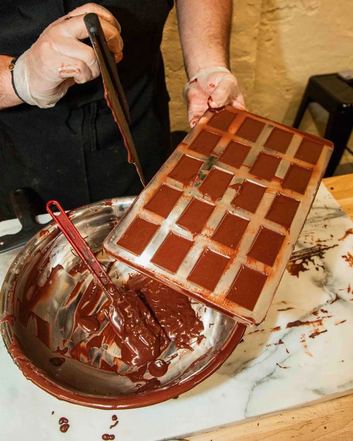 A person is pouring melted chocolate from a bowl into a mold during a bean-to-bar chocolate class.