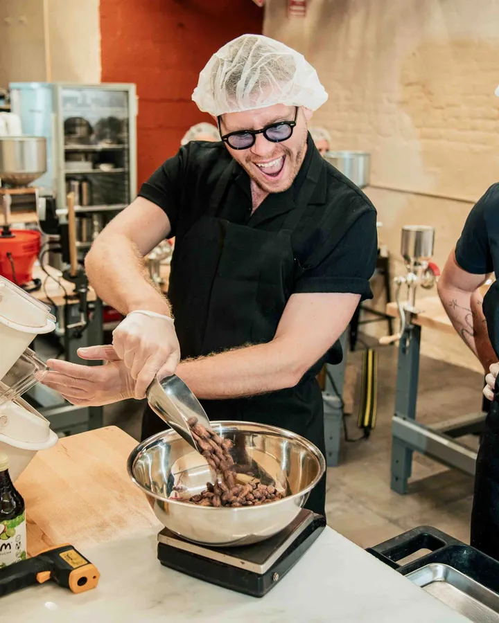 Participant joyfully measures cacao beans in a Bean-to-Bar chocolate class in New York City, wearing gloves and a hairnet.