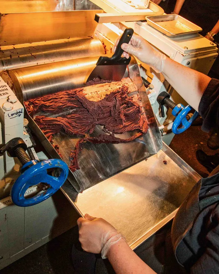 A hand scoops rich chocolate mixture from a machine during a Bean-to-Bar class in NYC.