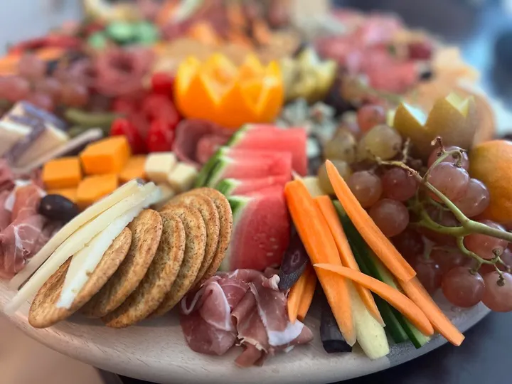 A vibrant cheese and charcuterie board with fruits, crackers, vegetables, and assorted meats.