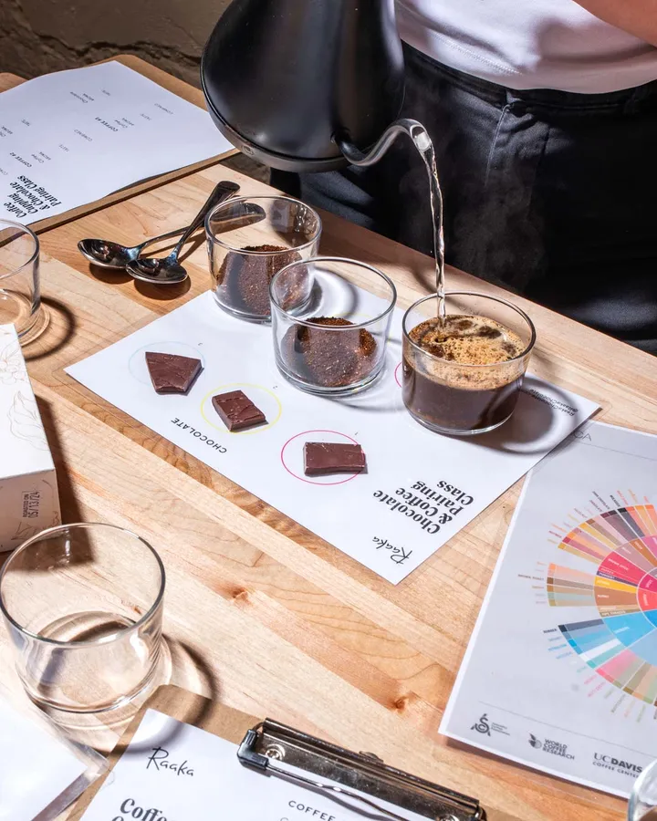 A person pours hot water over coffee grounds at a tasting event with chocolate pairings and tasting notes.