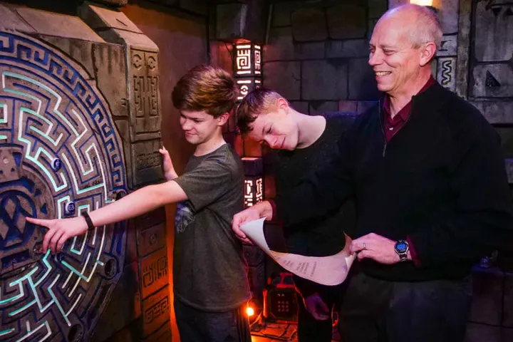 Three participants engage with a puzzle in an Escape Room, with expressions of concentration and teamwork.