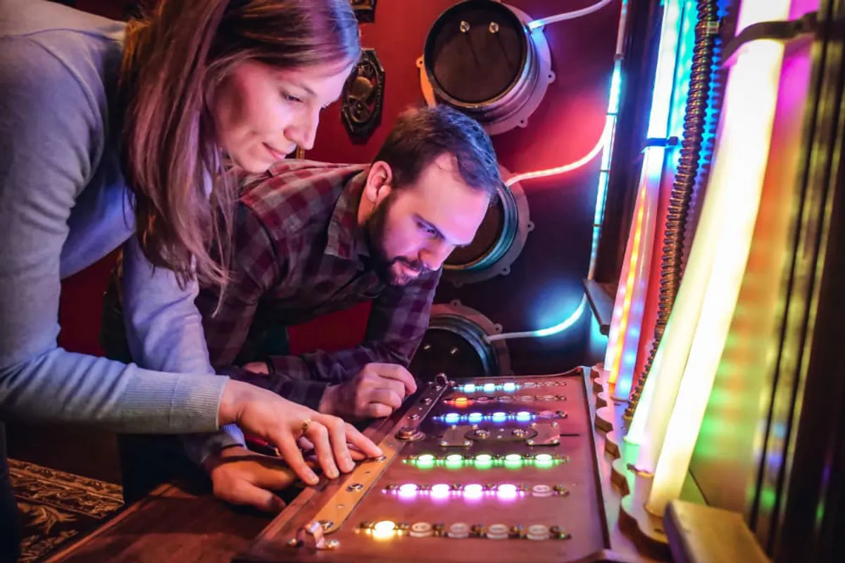 Two participants focus intently on a colorful control panel during an Escape Room activity in Louisville.