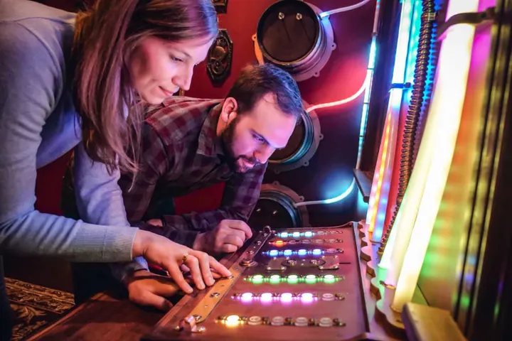 Two participants focus intently on a colorful control panel during an Escape Room activity in Louisville.
