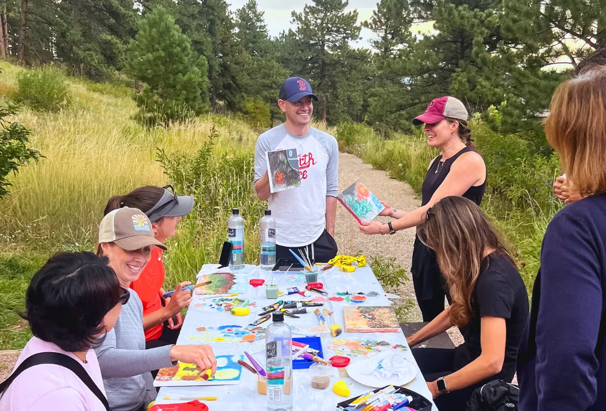 A group of people enjoying a painting activity outdoors on a hiking trail in Boulder.
