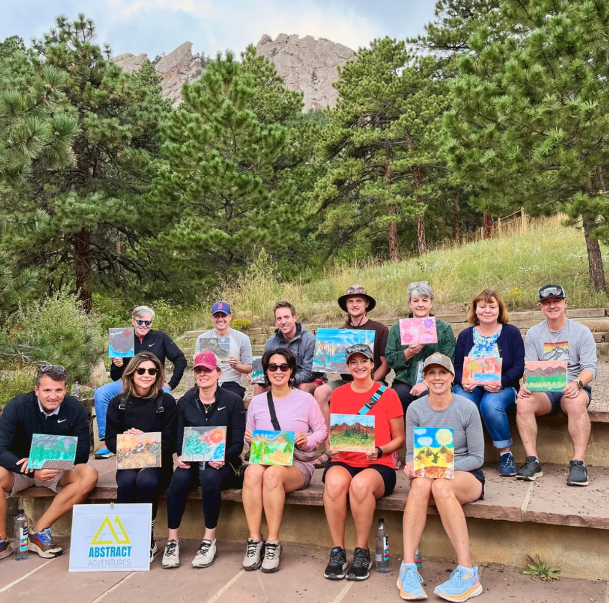 Group of participants holding their paintings after the Flatirons Hike and Paint activity in Boulder, surrounded by nature.