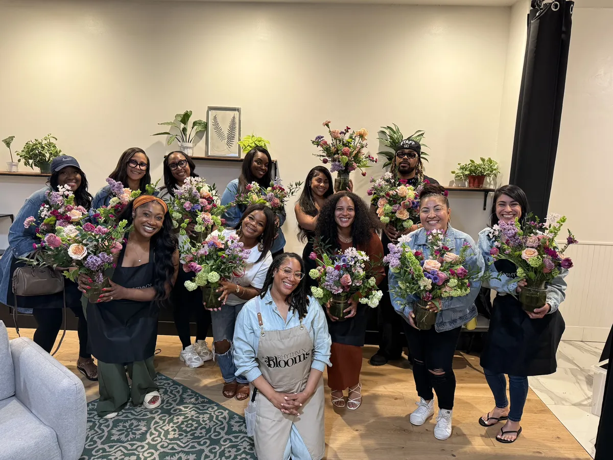 A diverse group of people poses with floral arrangements in a workshop setting in San Francisco.