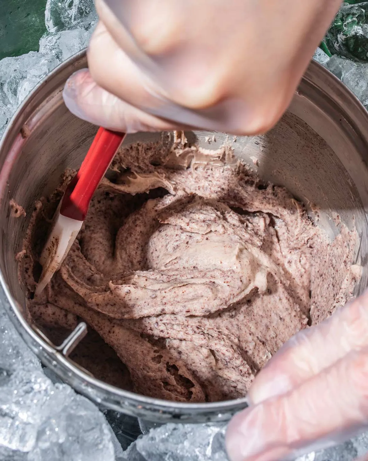 Hand stirring ice cream mixture in a metal bowl surrounded by ice, showcasing a team building activity in NYC.