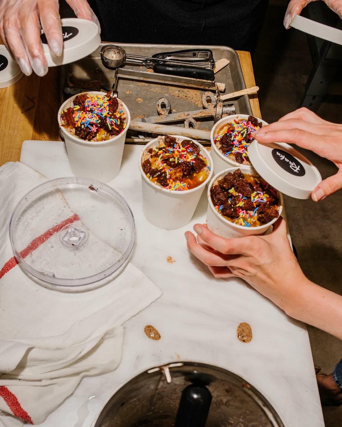 Hands prepare cups of ice cream topped with sprinkles during a team-building ice cream-making activity in NYC.