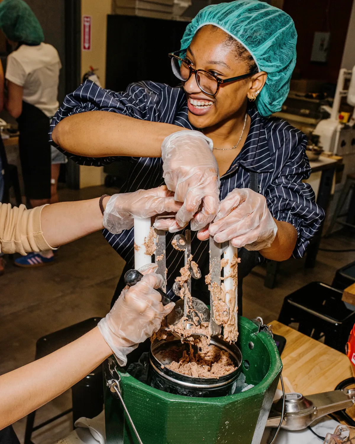 A person smiles while making ice cream, using a machine in a kitchen setting during a team-building activity.