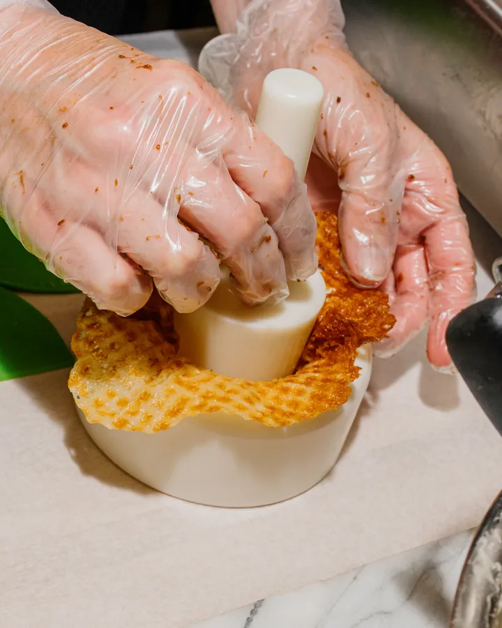 Hands in gloves shaping a waffle cone with a tool during an ice cream making team building activity in NYC.