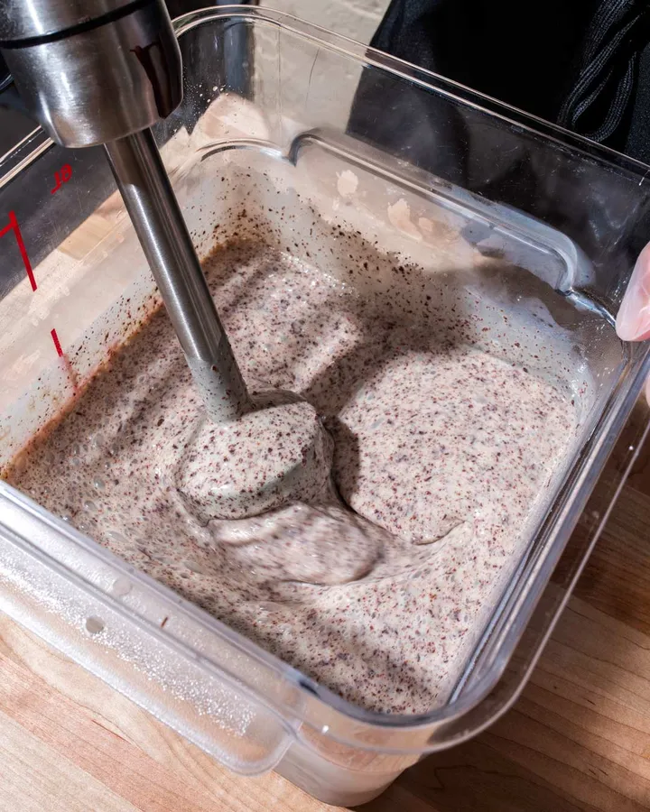 A hand blender mixes ice cream base in a clear container during an ice cream-making team activity in NYC.