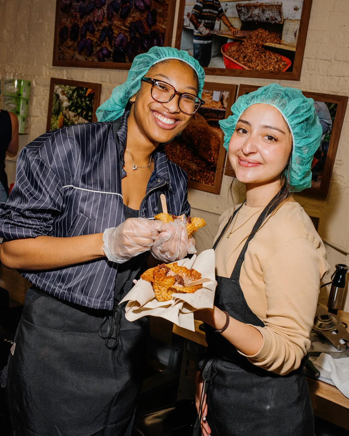 Two smiling women in aprons and hairnets hold homemade ice cream cones during a team-building ice cream-making activity.