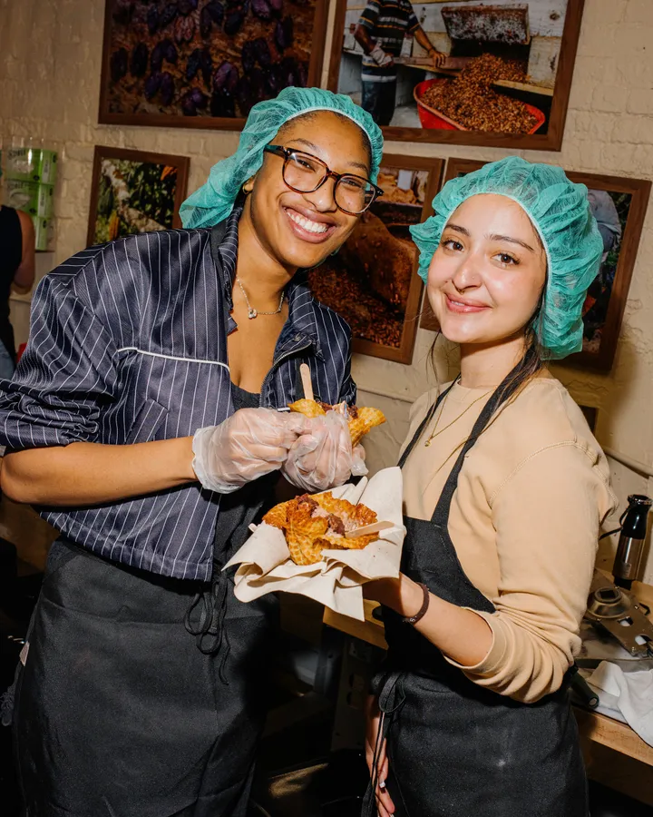 Two smiling women in aprons and hairnets hold homemade ice cream cones during a team-building ice cream-making activity.