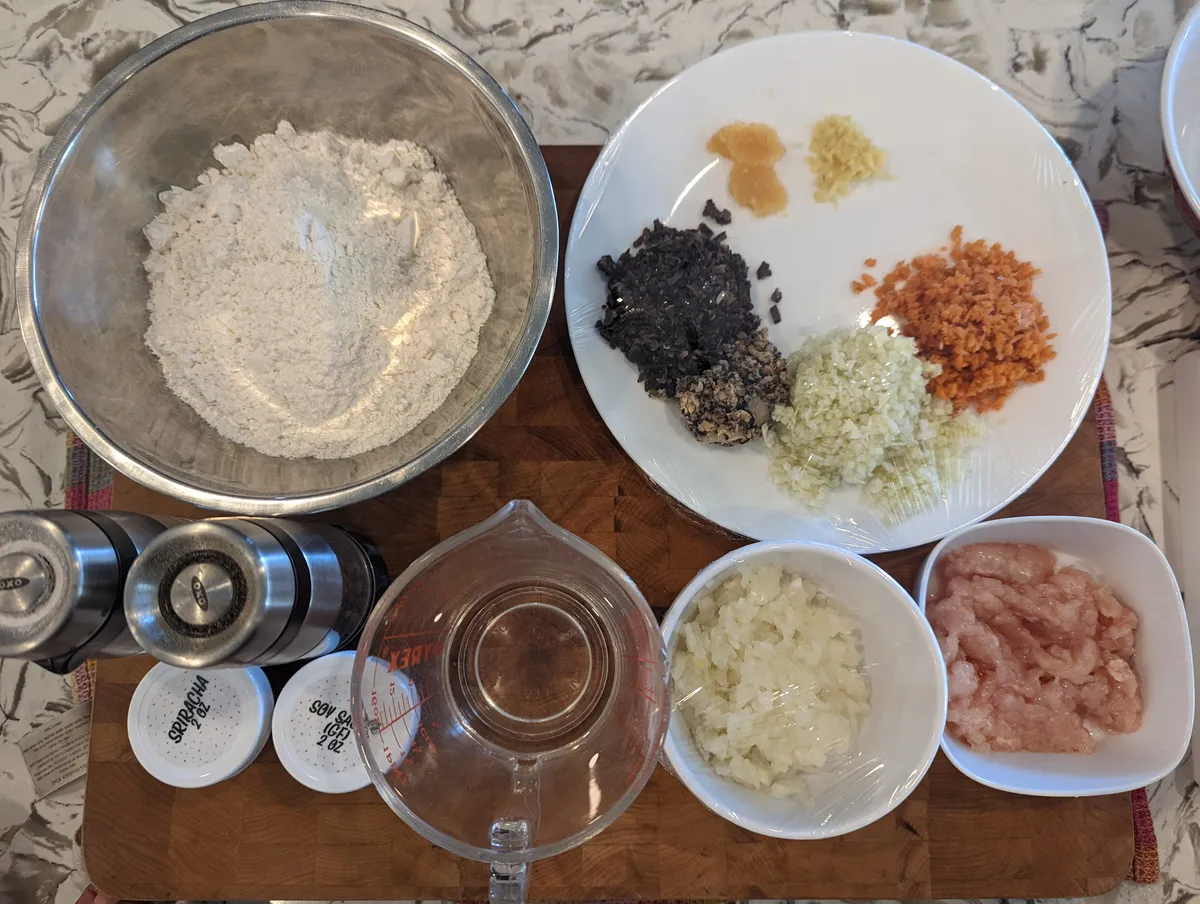 Ingredients for gyoza dumplings: flour, ground meat, vegetables, and condiments arranged on a countertop.