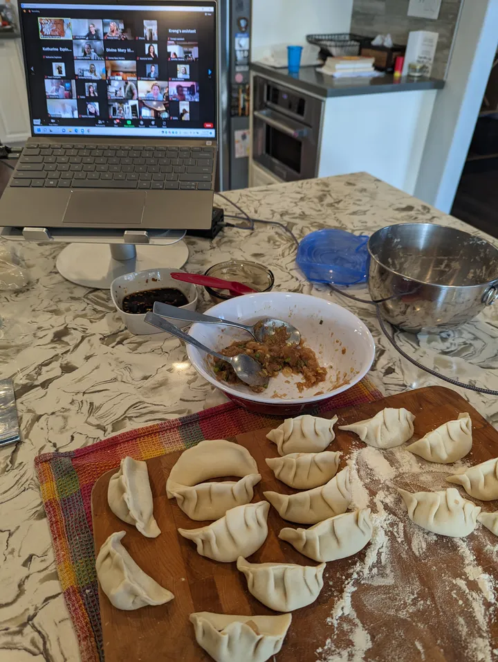 A tabletop scene showing freshly made gyoza dumplings and a laptop displaying a virtual cooking class.
