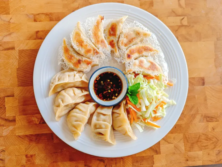 A plate of gyoza dumplings, including fried and steamed varieties, served with dipping sauce and fresh veggies.