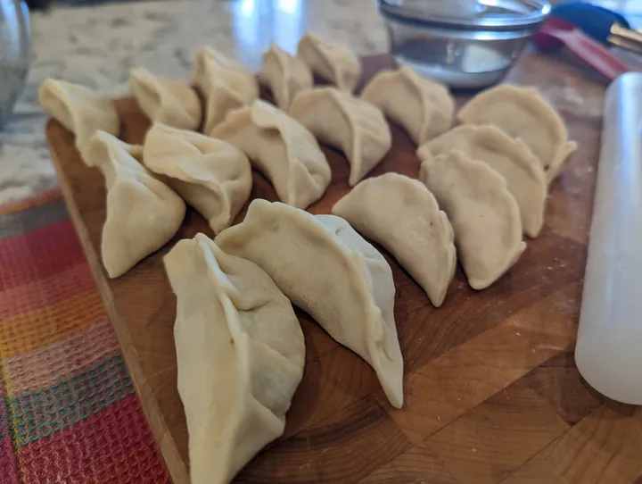 A wooden board displays neatly arranged uncooked gyoza dumplings, ready for cooking.