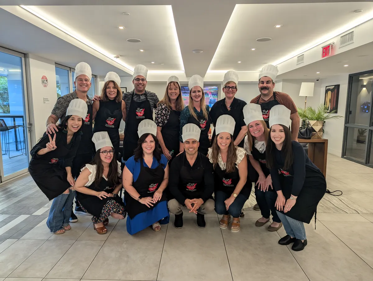 A group of people in chef hats and aprons poses together at a Japanese Gyoza Dumpling Class in San Diego.