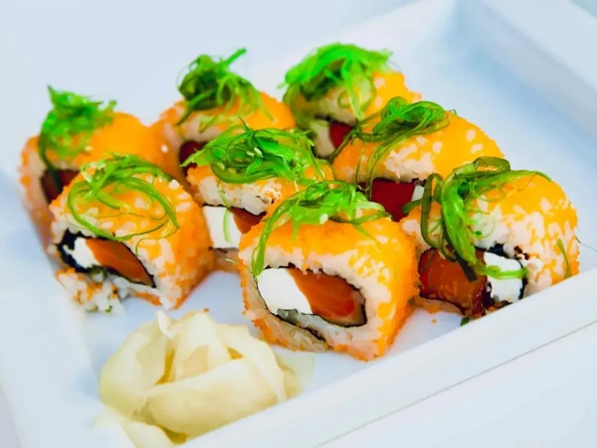 Colorful sushi rolls topped with green onions, served with pickled ginger on a white plate.