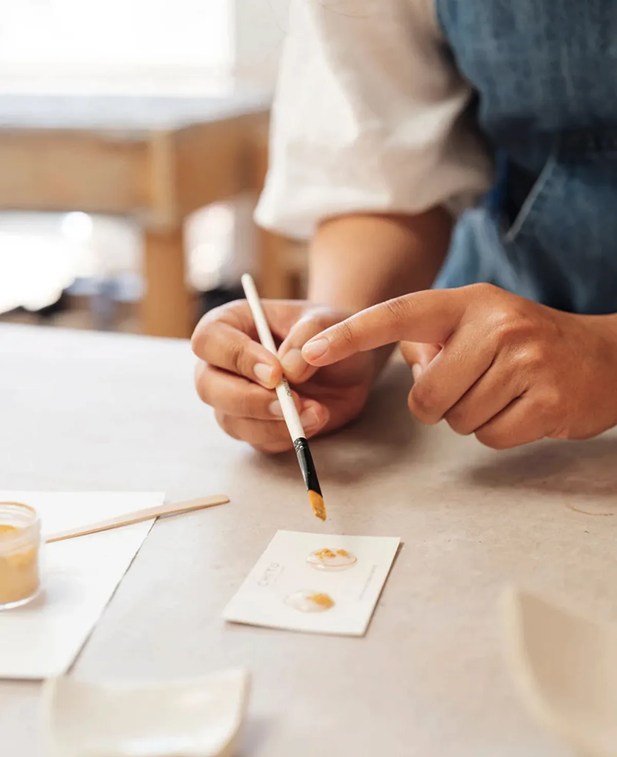 A hand holds a brush over two pieces of pottery, demonstrating the Kintsugi art technique in a Seattle workshop.
