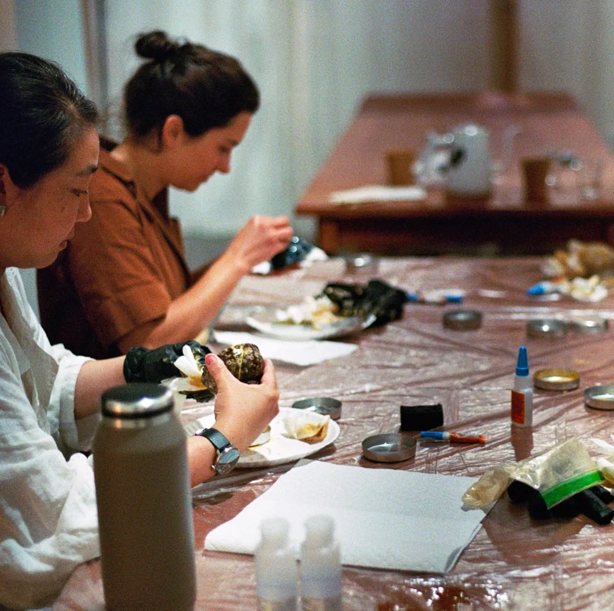 Participants in a Kintsugi class in Seattle work on repairing pottery at a table covered with supplies.