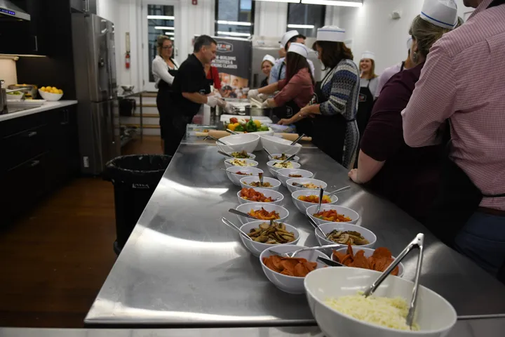 A group prepares food at a cooking event, featuring bowls of ingredients in a modern kitchen setting.