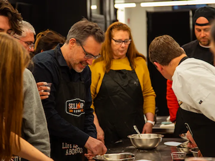 Group of people in aprons engaged in a Mexican cooking activity, focused on preparing ingredients together.