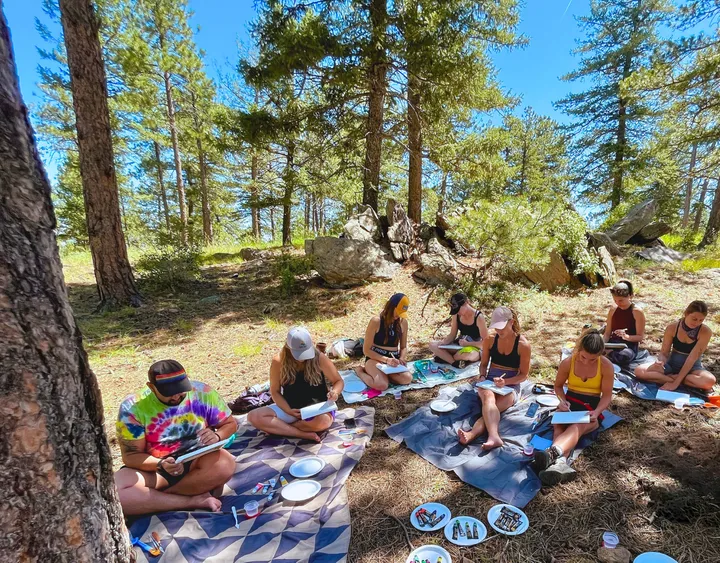Participants enjoying a creative outdoor session, painting on a sunny day surrounded by trees at Mt. Falcon.