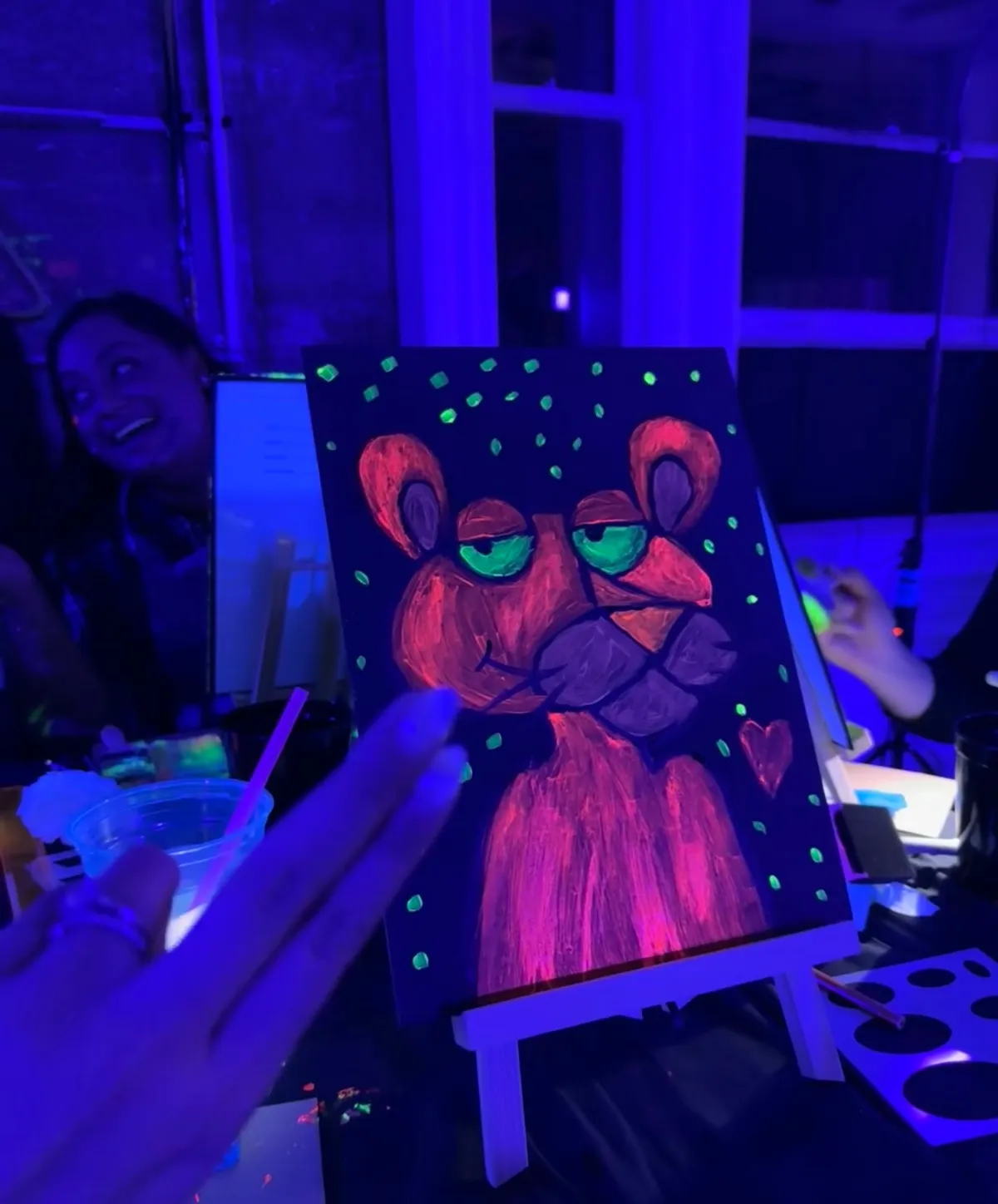 Neon painting of a cartoon-like lion with green eyes, surrounded by vibrant dots, at a fun Paint and Sip event.