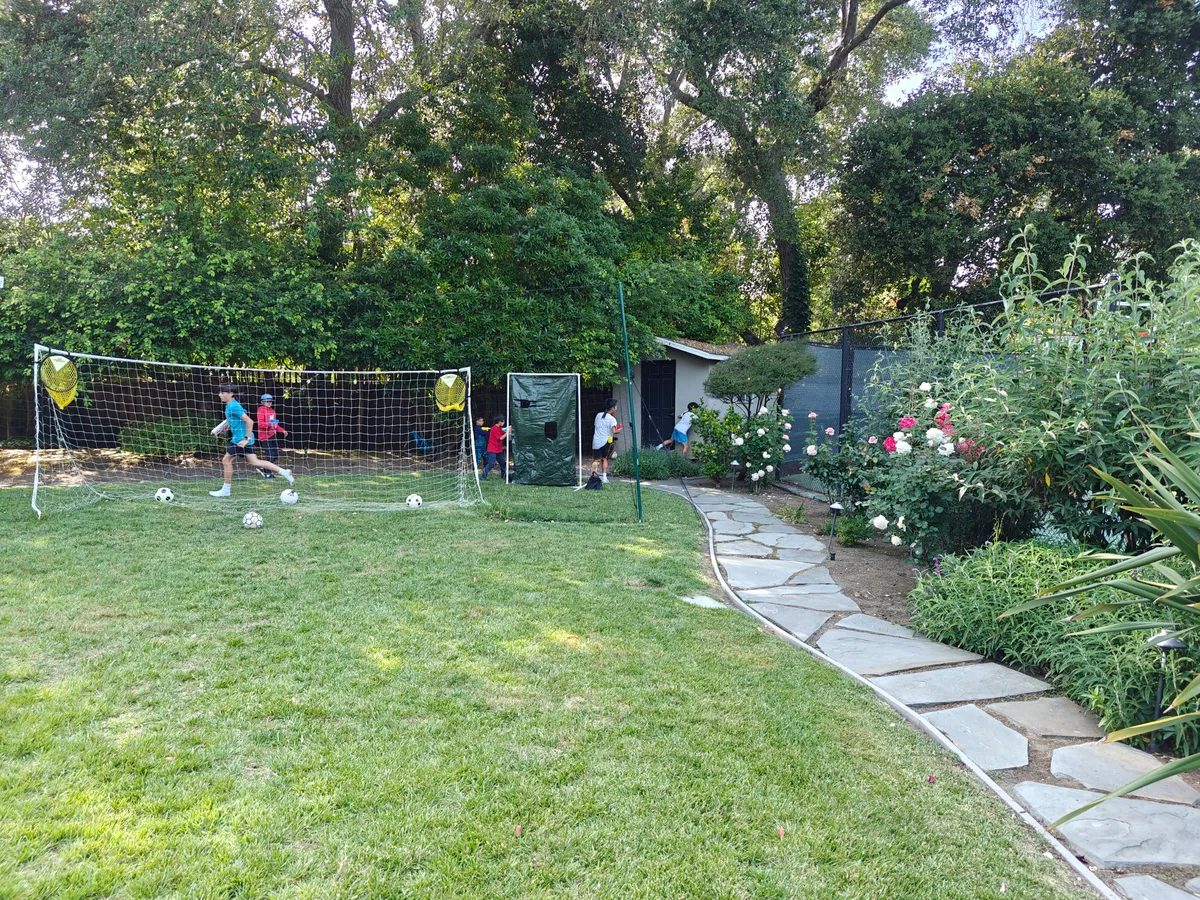 Kids participate in a Nerf Battle team building activity in a grassy outdoor area, surrounded by trees and flowers.