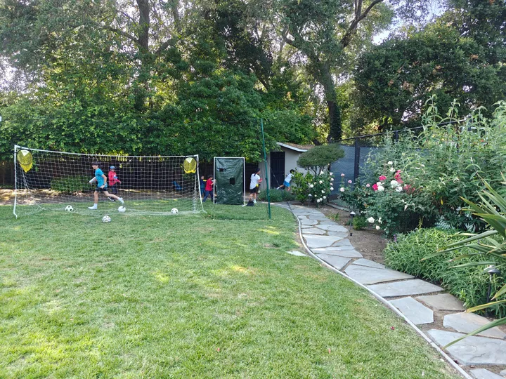 Kids participate in a Nerf Battle team building activity in a grassy outdoor area, surrounded by trees and flowers.