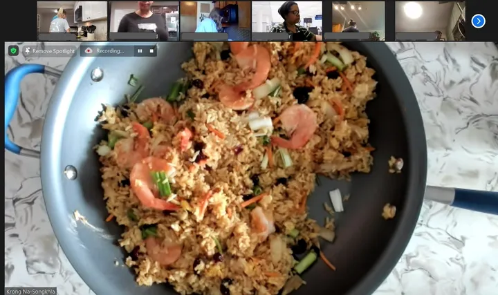 A close-up of pineapple fried rice with shrimp and vegetables, showing a cooking class on a video call in the background.