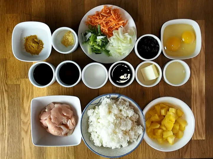 Ingredients for Pineapple Fried Rice: chicken, rice, pineapple, eggs, veggies, sauces, and seasonings arranged on a table.