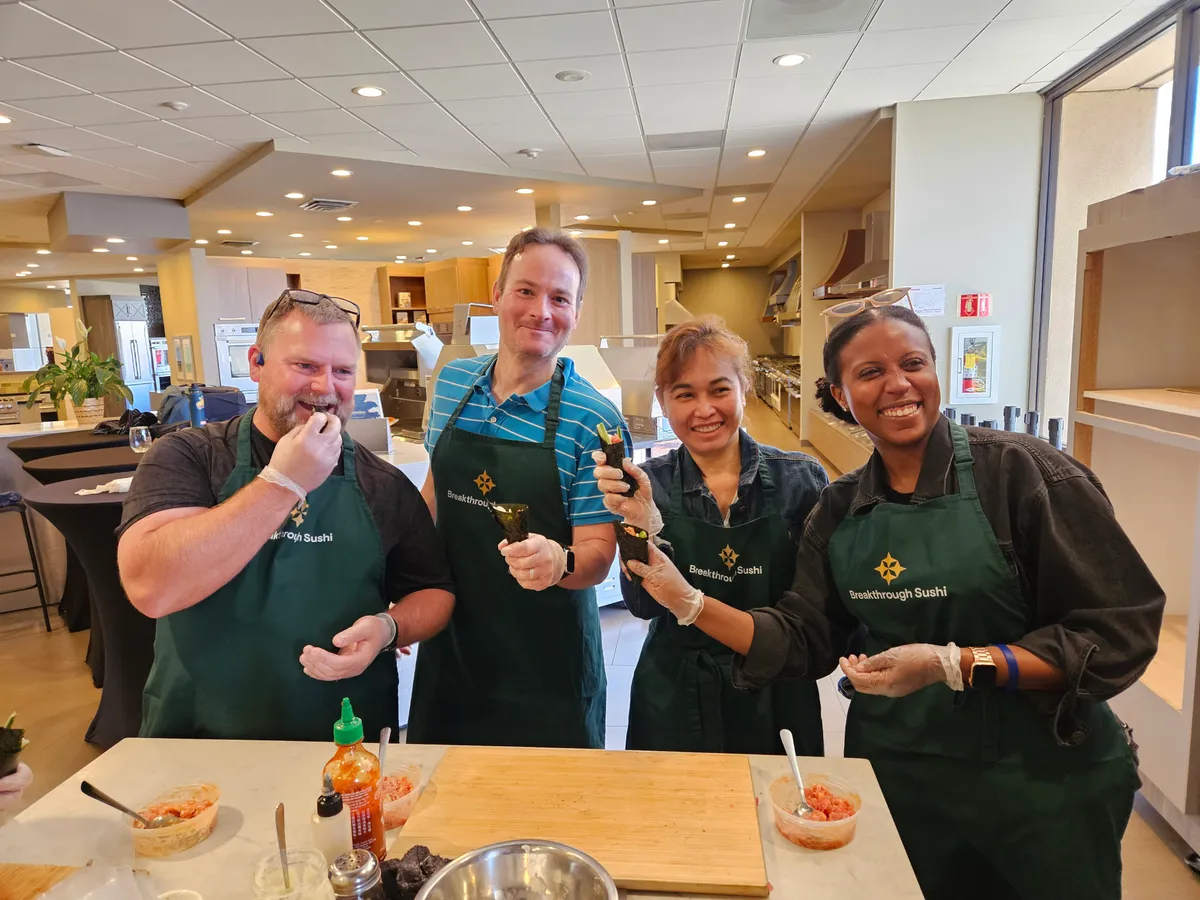 A group of four smiling participants in green aprons at a sushi-making workshop in San Francisco.