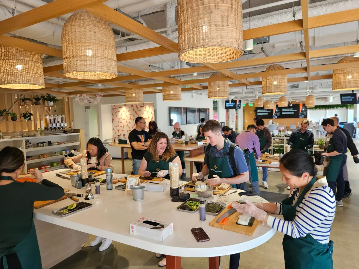 A group of people enjoying a sushi-making workshop, actively preparing sushi at a large communal table.