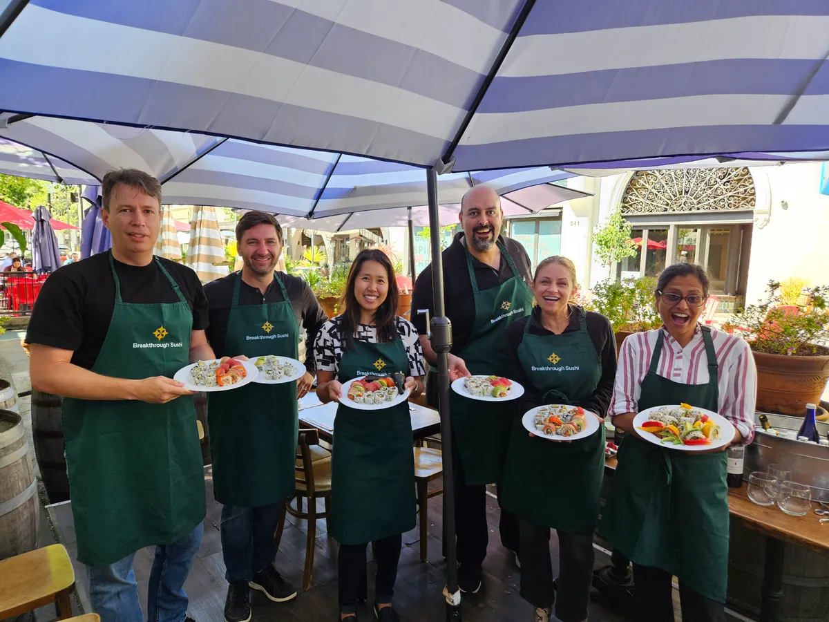 Group of six participants holding sushi plates at a sushi-making workshop under colorful umbrellas in San Francisco.