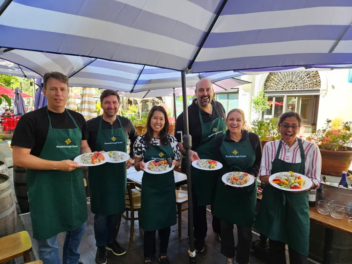 Group of six participants holding sushi plates at a sushi-making workshop under colorful umbrellas in San Francisco.