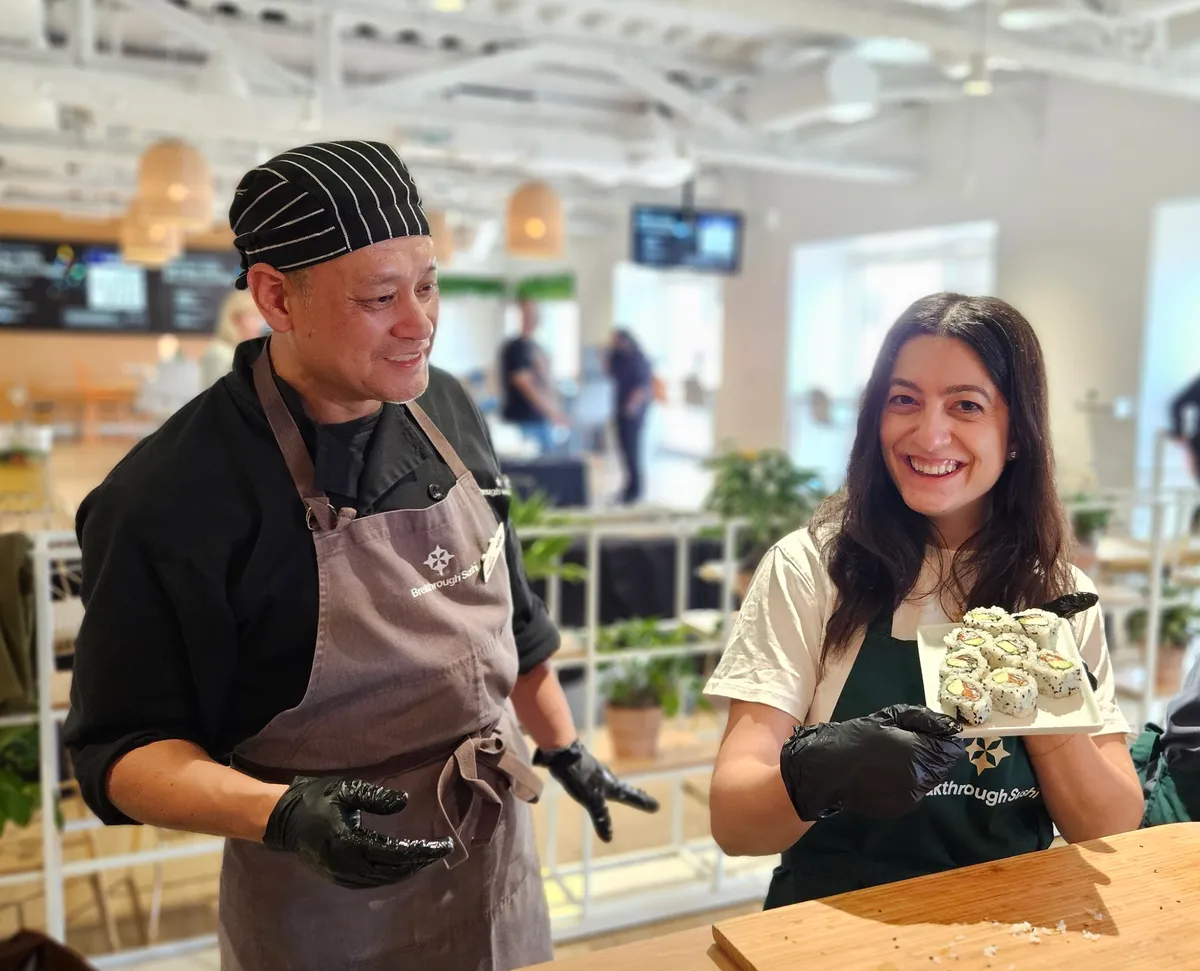 Participants enjoy a sushi-making workshop, with a chef and a smiling lady holding a plate of sushi.