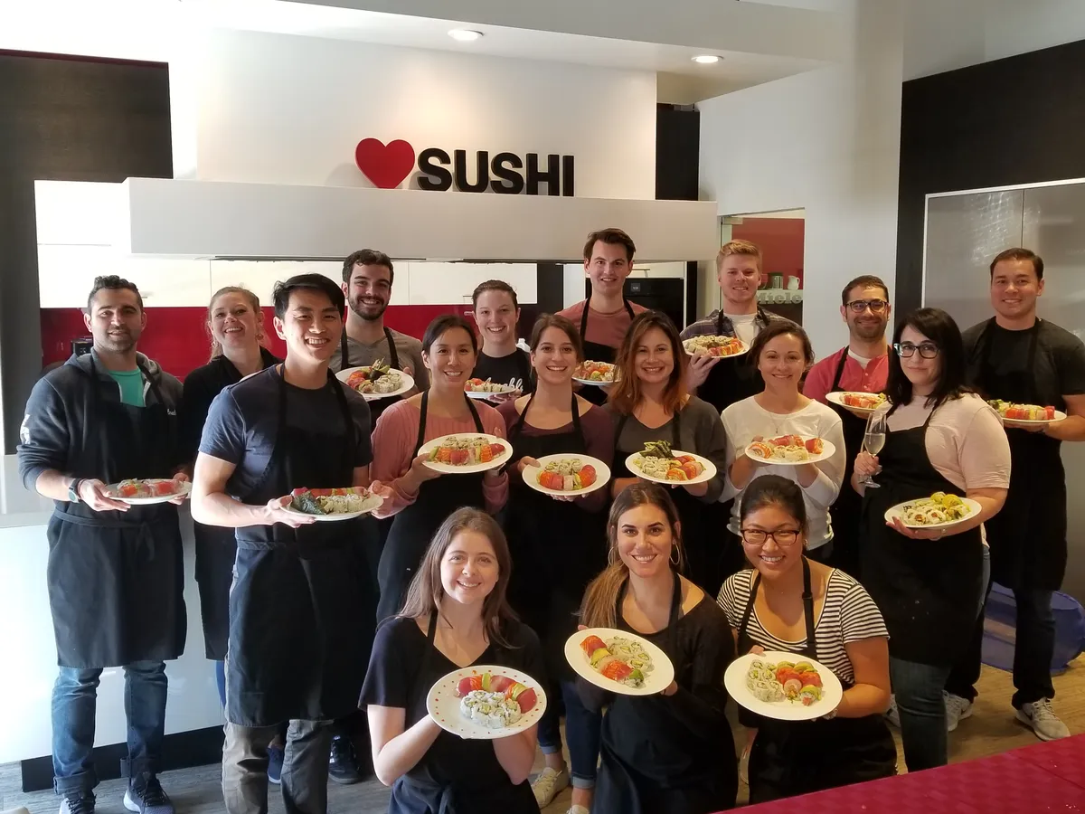 Group photo of participants holding sushi plates at a workshop in San Francisco, with a "Love Sushi" sign in the background.