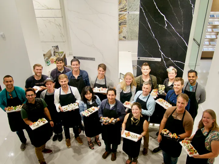 A group holds sushi creations during a team-building activity in a bright workshop space.
