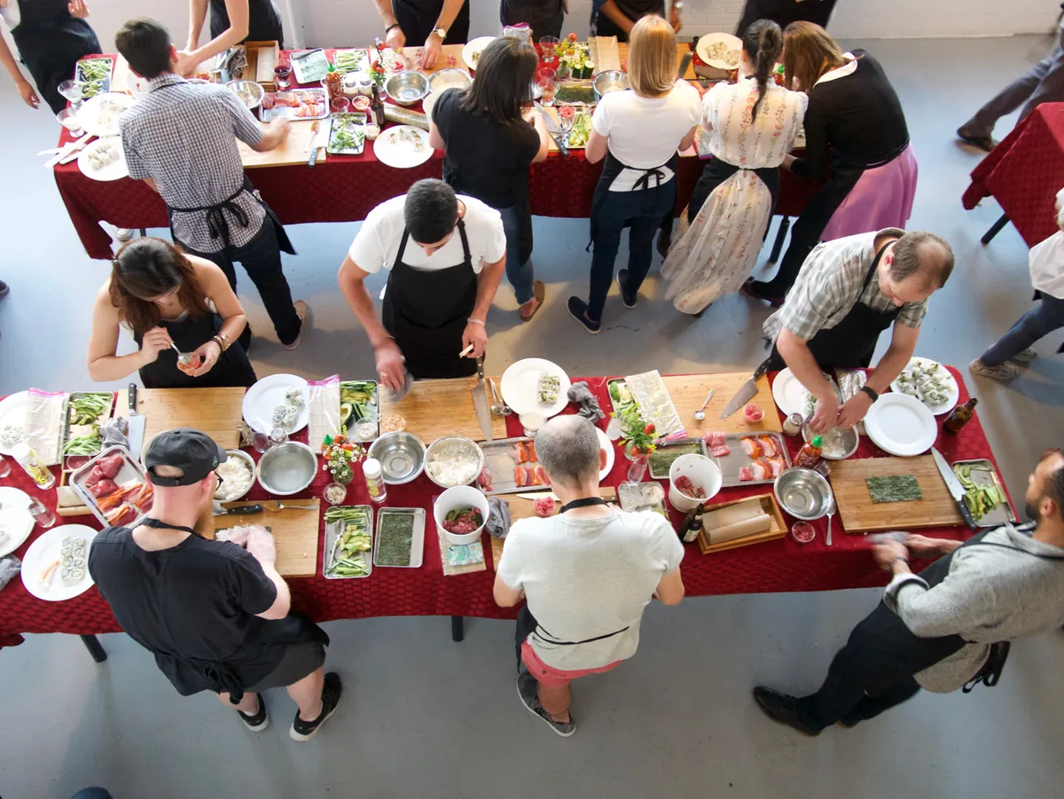 Team members participate in a sushi-making workshop, preparing ingredients at tables filled with fresh produce and supplies.