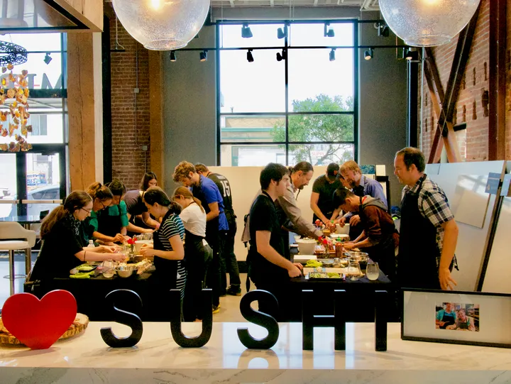 Group of people participating in a sushi-making workshop in San Francisco, focused on preparing sushi at a counter.