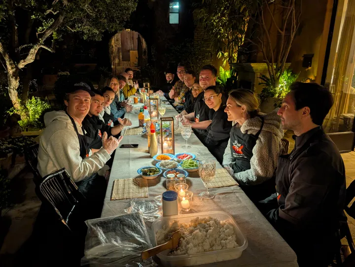 Group of people at a long table during a Sushi Rolling Class in San Diego, with sushi ingredients and candles.