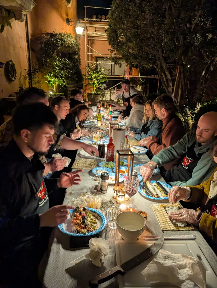 A group of people at a long table enjoying a sushi rolling class outdoors at night in San Diego.