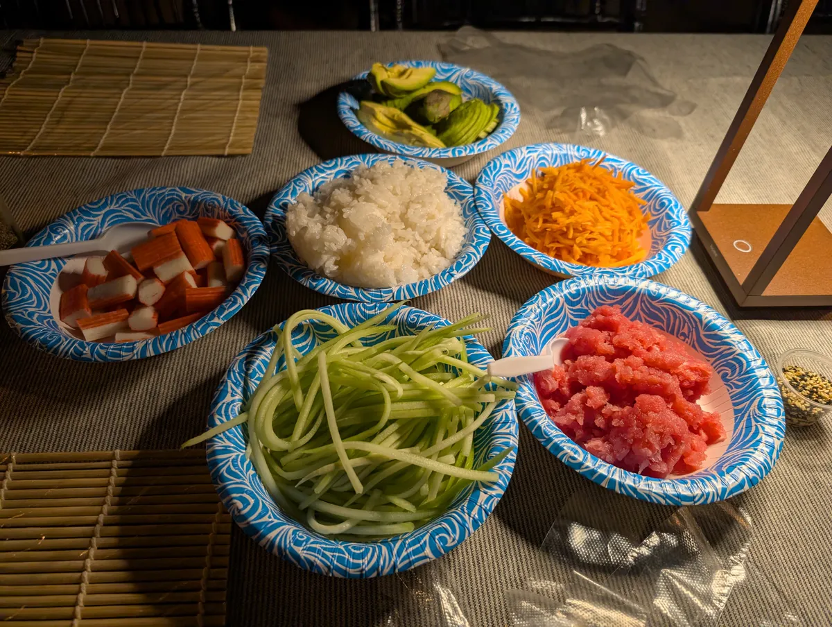 Ingredients for sushi rolling: crab, rice, cucumber, avocado, tuna, and shredded carrots on decorative plates.
