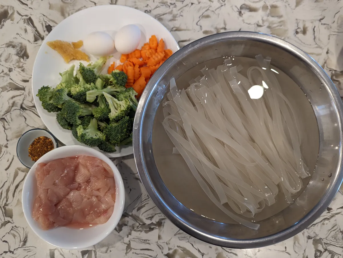 Ingredients for Pad-See-Ew: soaked rice noodles, chicken, broccoli, carrots, eggs, ginger, and seasonings.